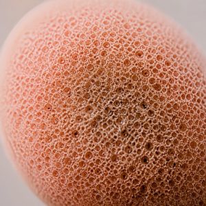 Hands rinsing a pink makeup sponge under running water, part of a clean girl makeup routine care step